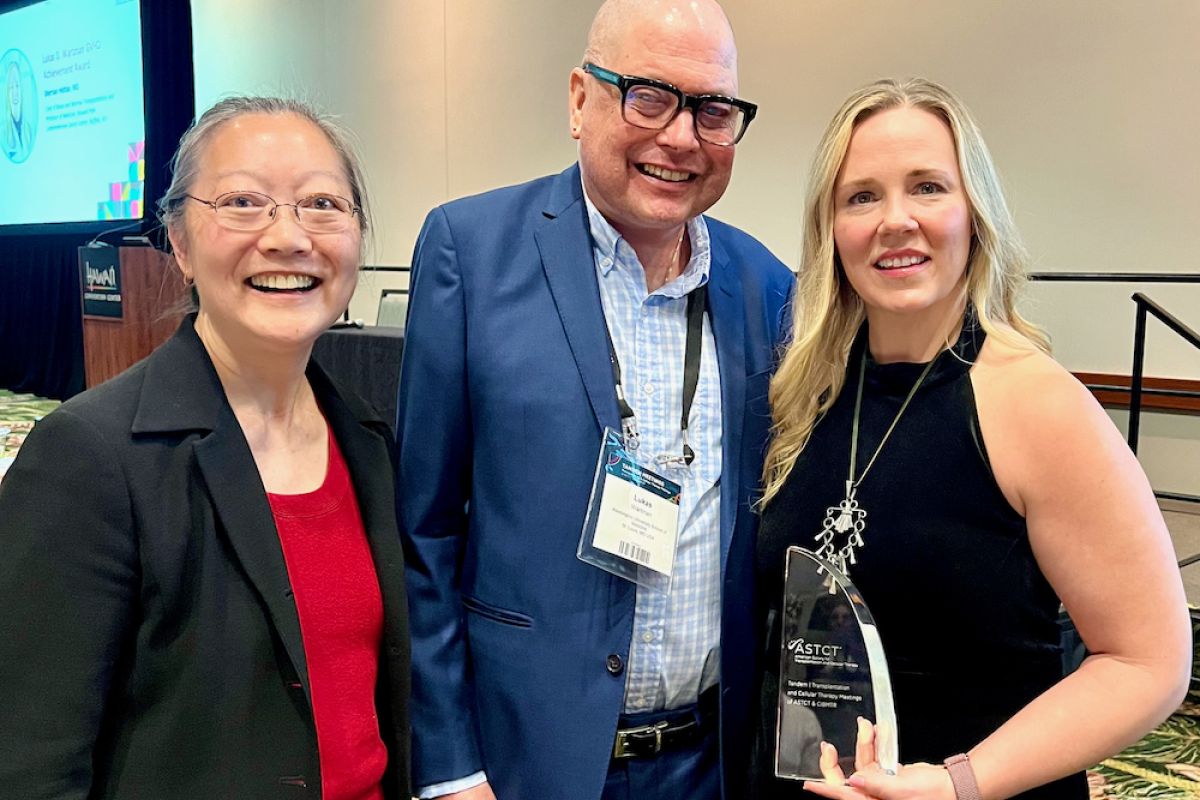 A woman holding a glass award stands to right of a man and a woman